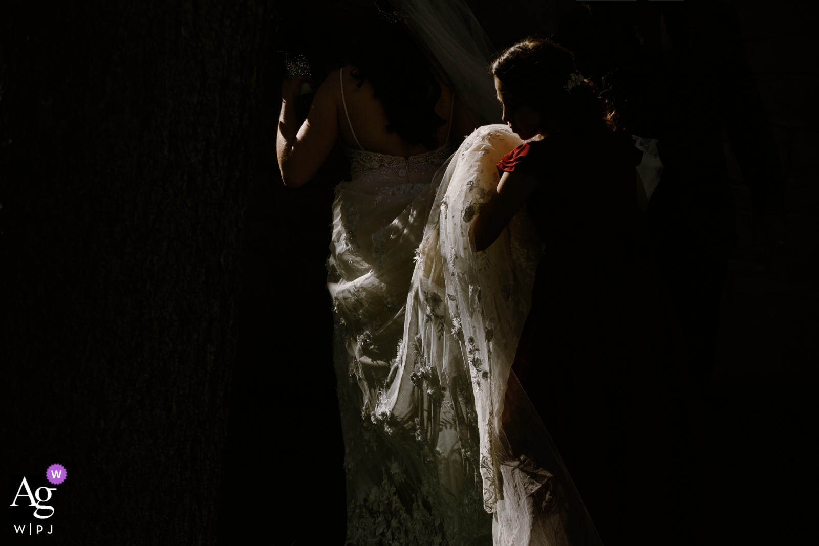 The bride and groom shared a romantic moment at their Montana wedding, the groom tenderly holding her dress against a darkened background.