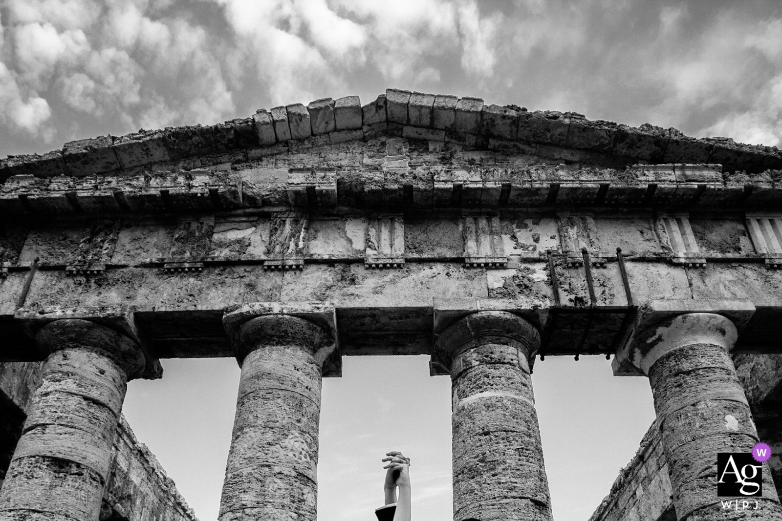 La novia y el novio posaron para una imagen atemporal en blanco y negro, con las manos apretadas de alegría mientras estaban de pie frente a la antigua estructura de columnas.