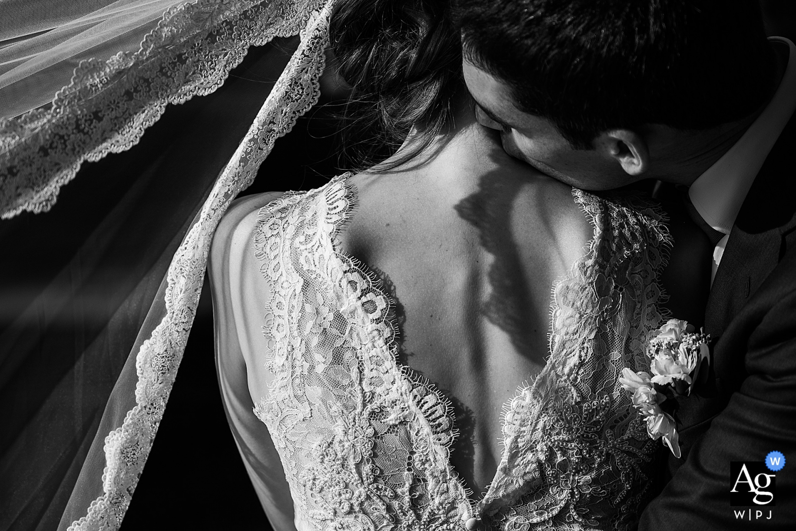 In this stunning black and white image, the groom tenderly kisses the bride's neck as her veil gracefully dances in the wind of sheer romance at their Antwerpen wedding