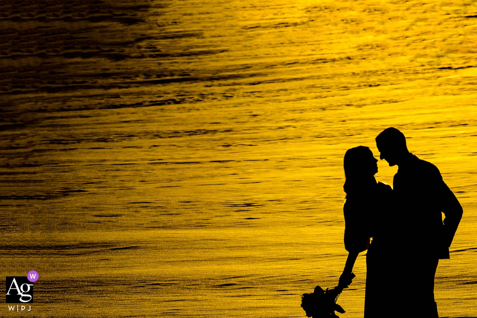 An einem Hochzeitstag wurde in Edmonton, Alberta, die Silhouette einer Braut und eines Bräutigams vor der Sonnenuntergangskulisse aus Wasser oder Schnee aufgenommen