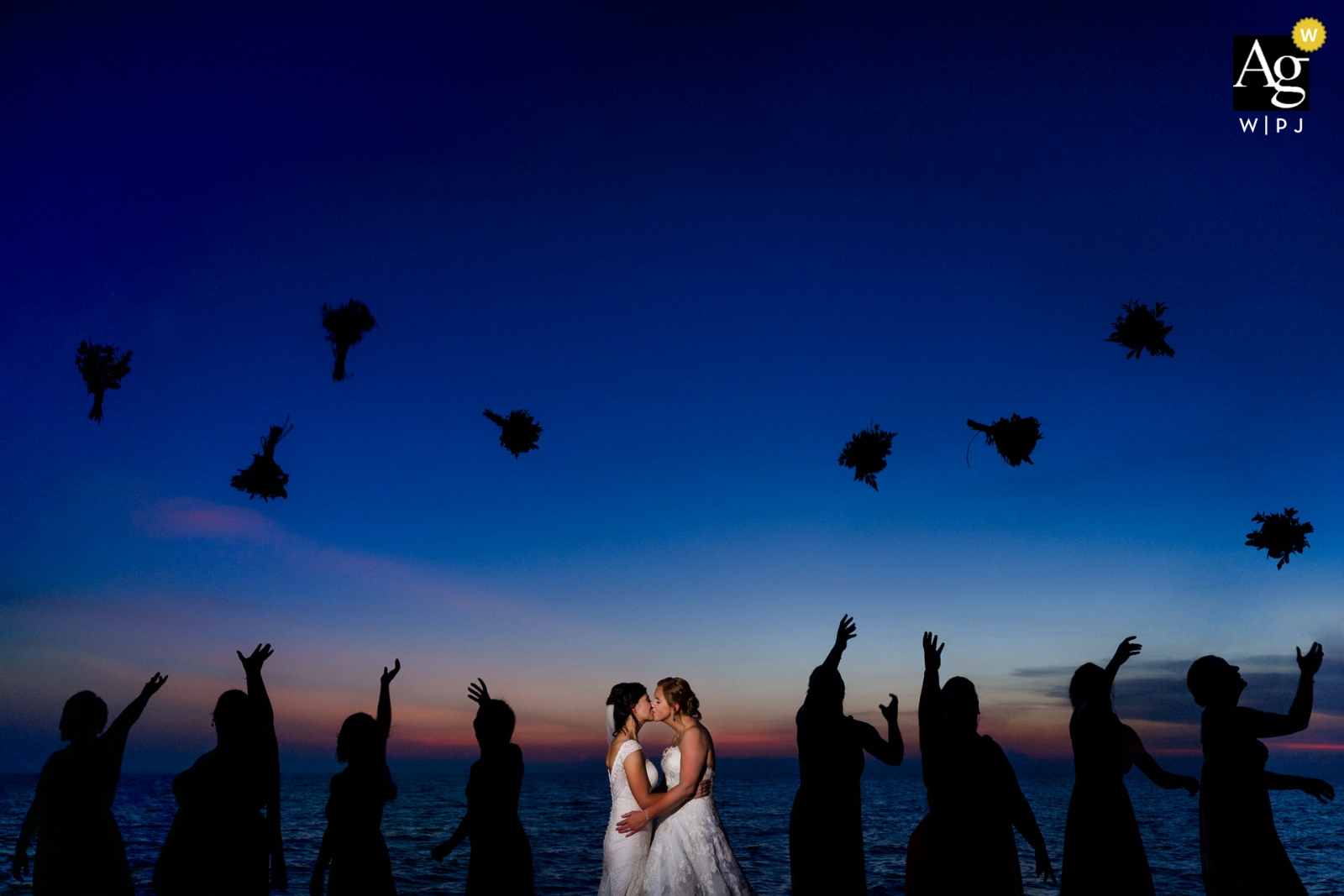 Uma sessão de retratos com uma noiva jogando flores para o alto ao entardecer atrás de um casal se beijando ocorreu em Phu Quoc, Vietnã