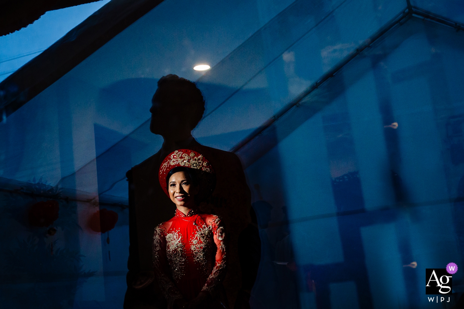 Une photo de mariage prise au lac Tahoe présente une mariée éthérée vêtue d'une robe rouge, avec la silhouette de son marié superposée de manière éclatante sur la vitre au-dessus d'elle