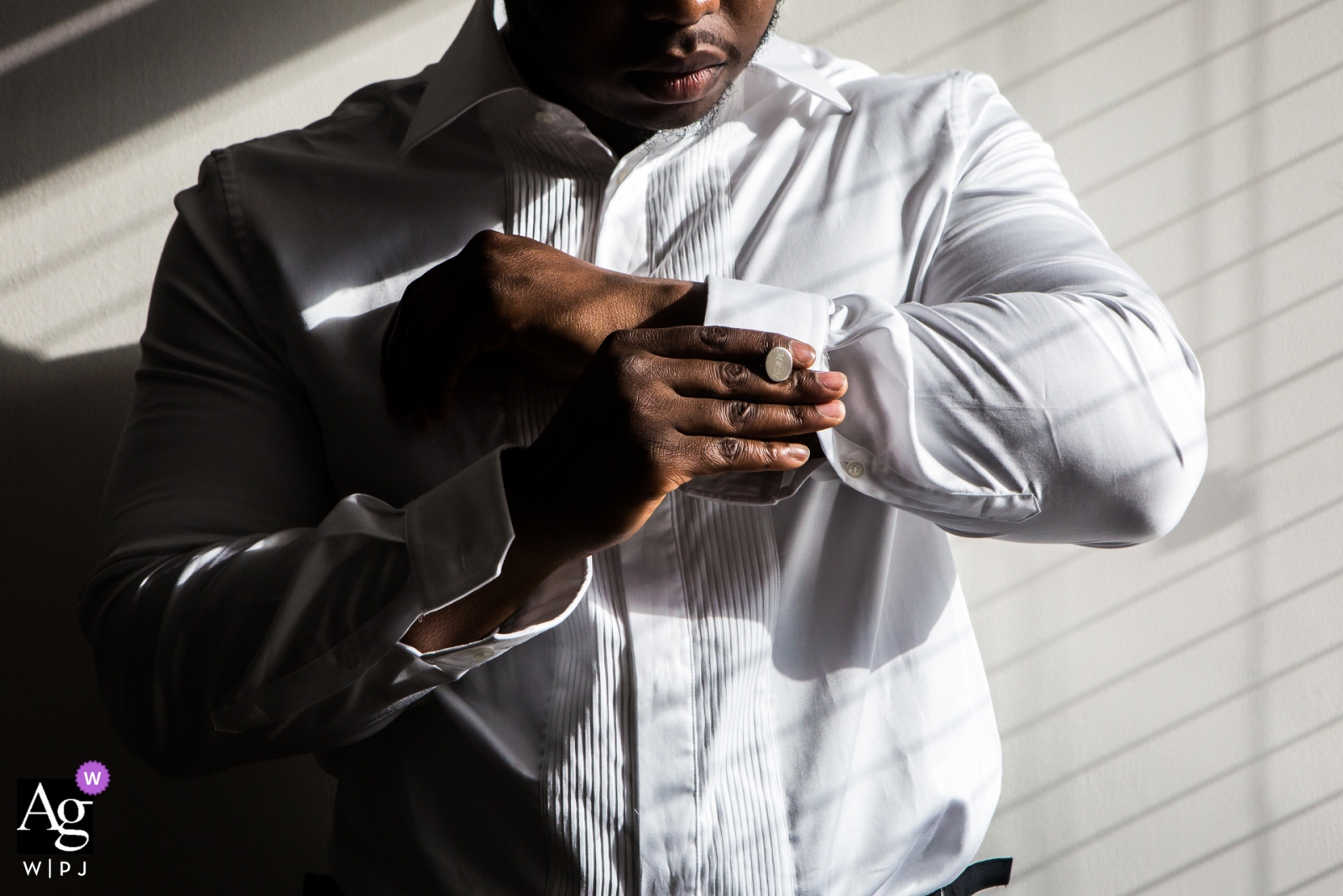 The groom was getting ready by fixing cuflinks in the sunlight coming through a window at a wedding venue in London