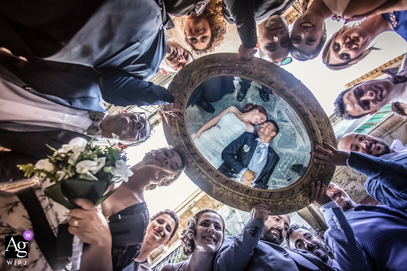 La novia y el novio se reflejan en un espejo sostenido por la fiesta nupcial en una impresionante imagen de boda tomada en Il Mirto, Rosolini, Italia.