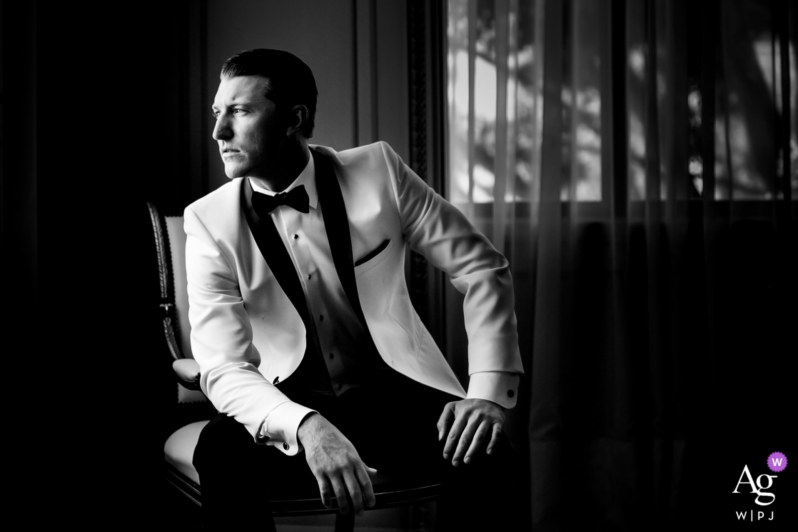 La fotografía en blanco y negro tomada en San Diego, California, captura a un novio sentado en una silla, lo que brinda una visión perspicaz del día de la boda.