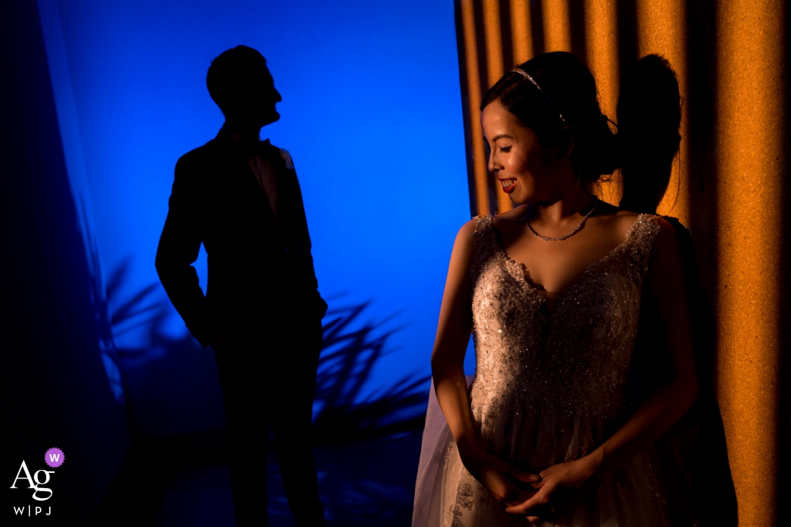 Esta foto de boda tomada en Phuket, Tailandia, presenta una ingeniosa combinación de iluminación cálida en la novia y una silueta del novio contra un cielo azul oscuro.