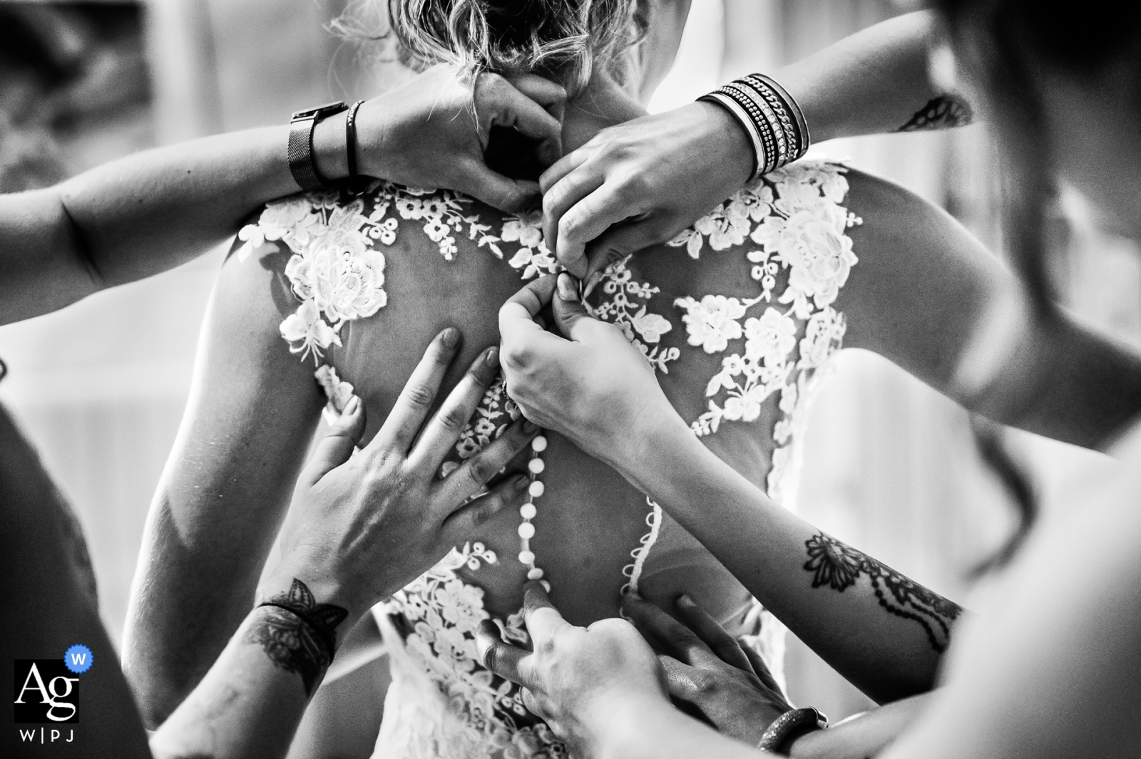 A black and white image from Chateau d'Aubiac, France, shows numerous hands assisting the bride with the buttons on her dress in preparation for the upcoming wedding