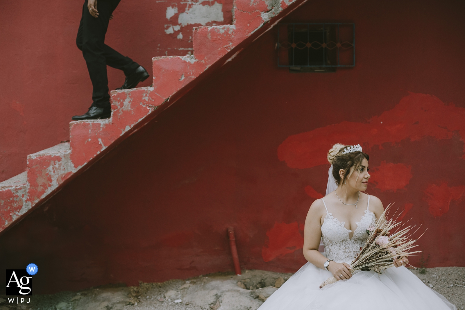 The groom is seen descending the stairs to join his bride, who is seated with her bouquet, for a beautiful wedding portrait