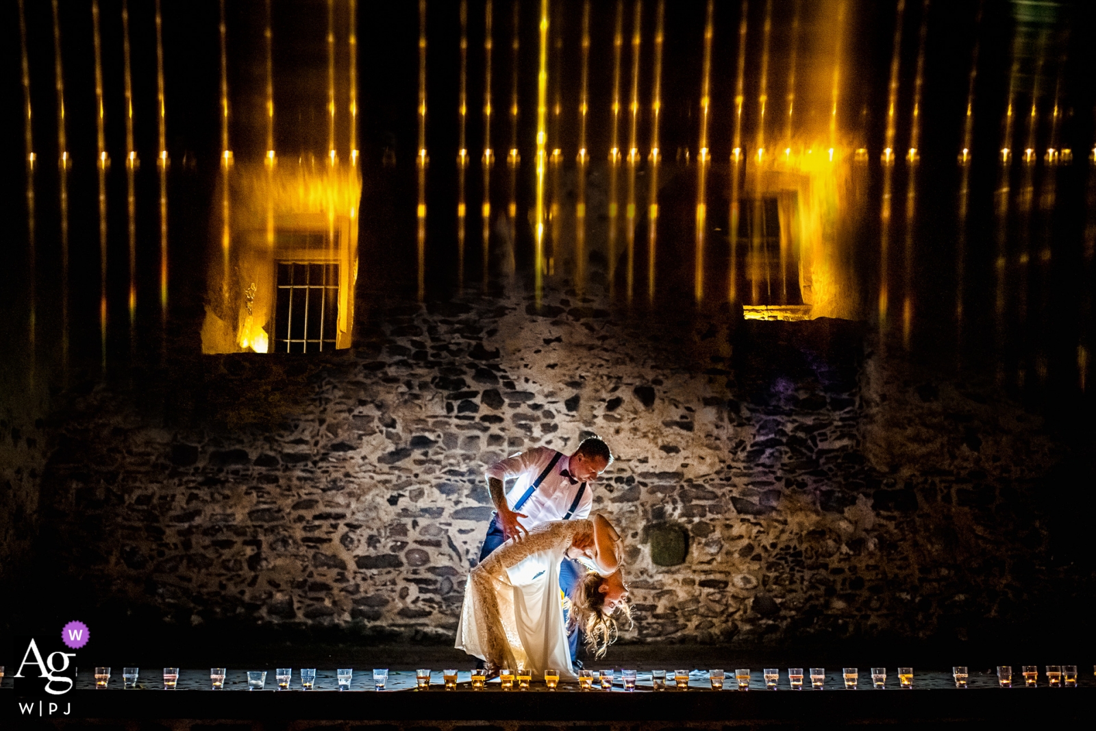 La novia y el novio se sumergieron frente a la pared de piedra iluminada de Schloss Romrod, creando un hermoso retrato nocturno.