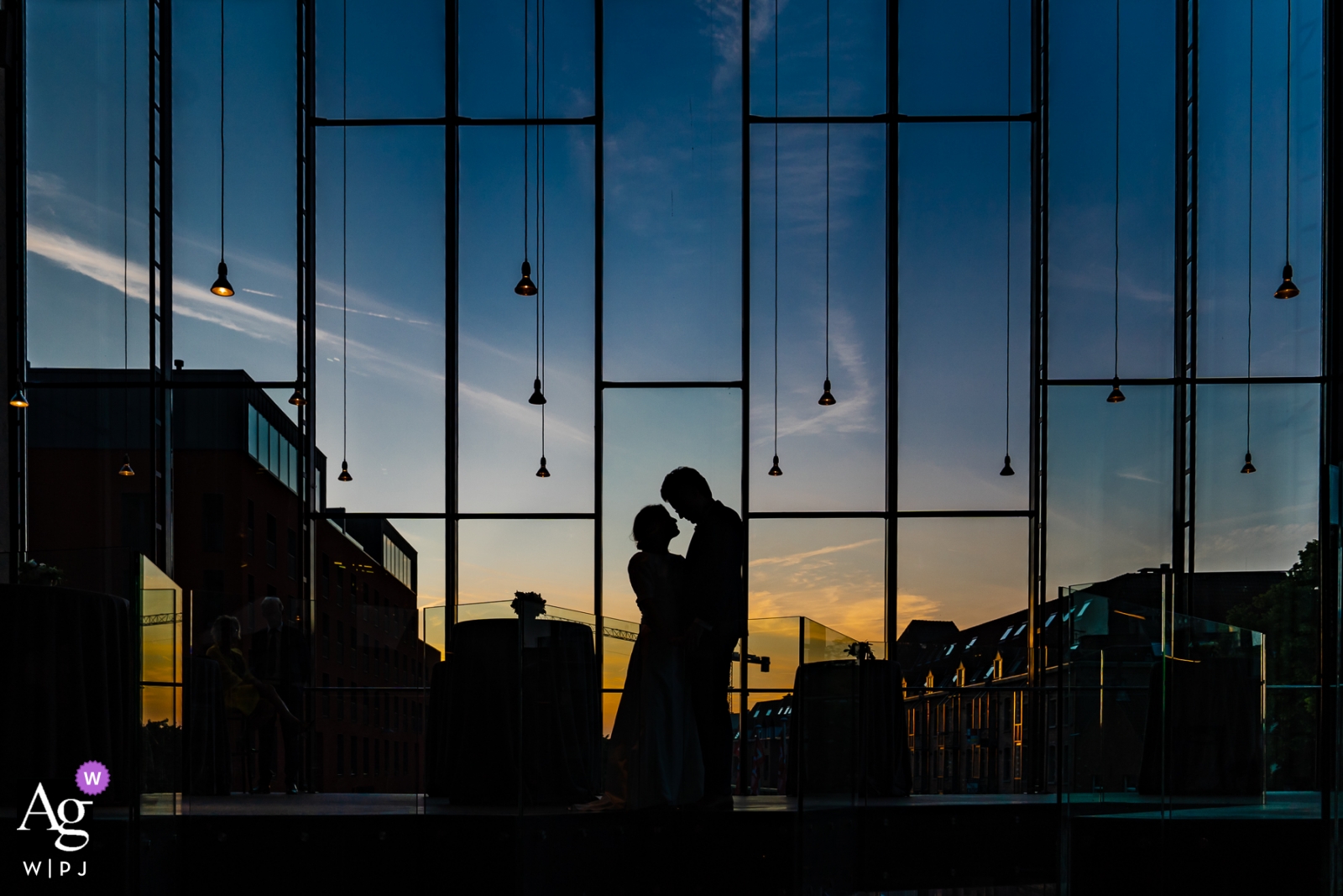 Foto por: <a href="https://www.wpja.com/photos/artistic-wedding-photographers/2528761"> Simon Leclercq - Leuven Vlaams Brabant Este retrato de silhueta da noiva e do noivo em frente a uma parede de vidro ao pôr do sol foi desenhado por um fotógrafo de casamento de Flandres