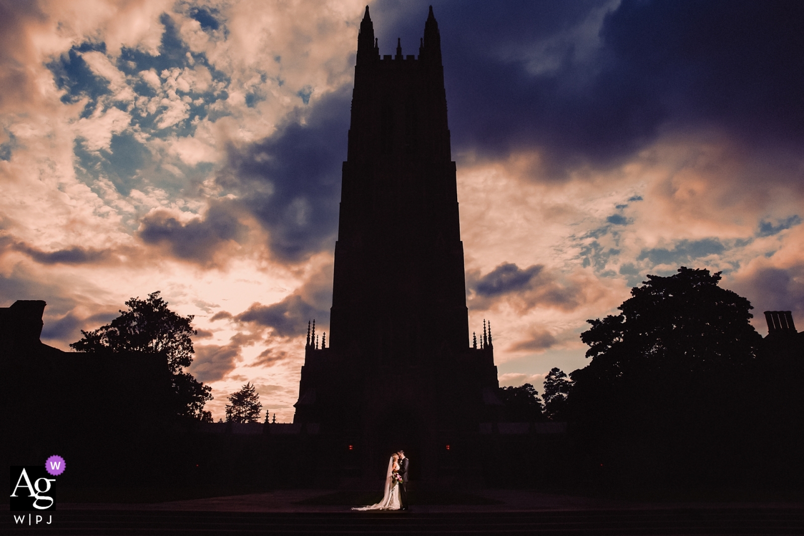 Foto von: <a href="https://www.wpja.com/photos/artistic-wedding-photographers/2544116"> Joe Payne - Raleigh North Carolina North Carolina-Hochzeitsporträt der Braut und des Bräutigams außerhalb Dukes Chapel, beleuchtet durch Röhrenblitz für Schattenbild der Kirche
