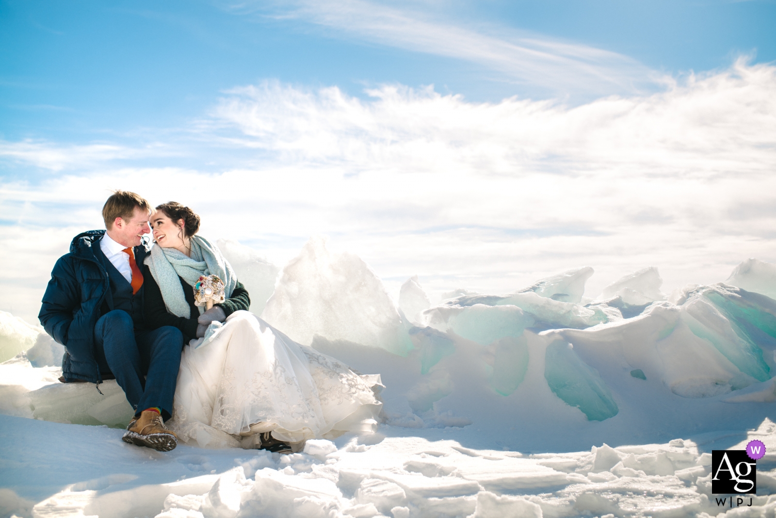 Foto von: <a href="https://www.wpja.com/photos/artistic-wedding-photographers/2549344"> Viara Mileva - Bath Ontario Braut und Bräutigam sitzen für eine Pause auf den eisigen Ufern des Ontariosees für ein Hochzeitsporträt