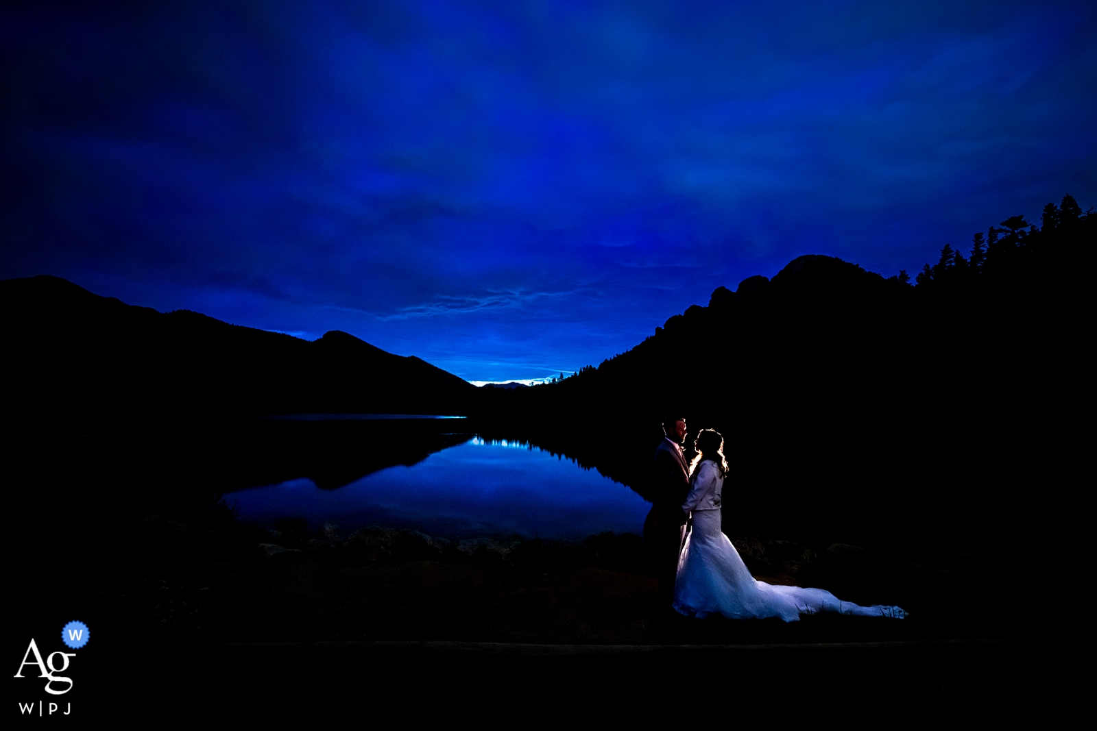 Foto von: <a href="https://www.wpja.com/photos/artistic-wedding-photographers/2556565"> Jesse La Plante - Boulder Colorado Blaues Stundenporträt der Braut und des Bräutigams durch See. Lily Lake - Rocky Mountain Nationalpark