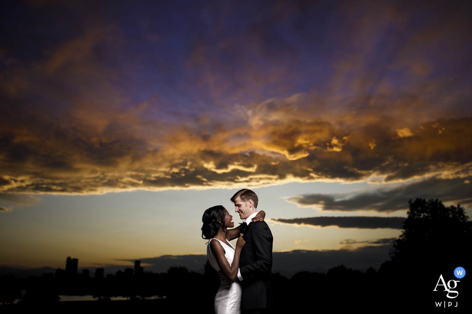 La novia y el novio toman una foto juntos mientras el sol se pone detrás de ellos en el Museo de Naturaleza y Ciencia de Denver