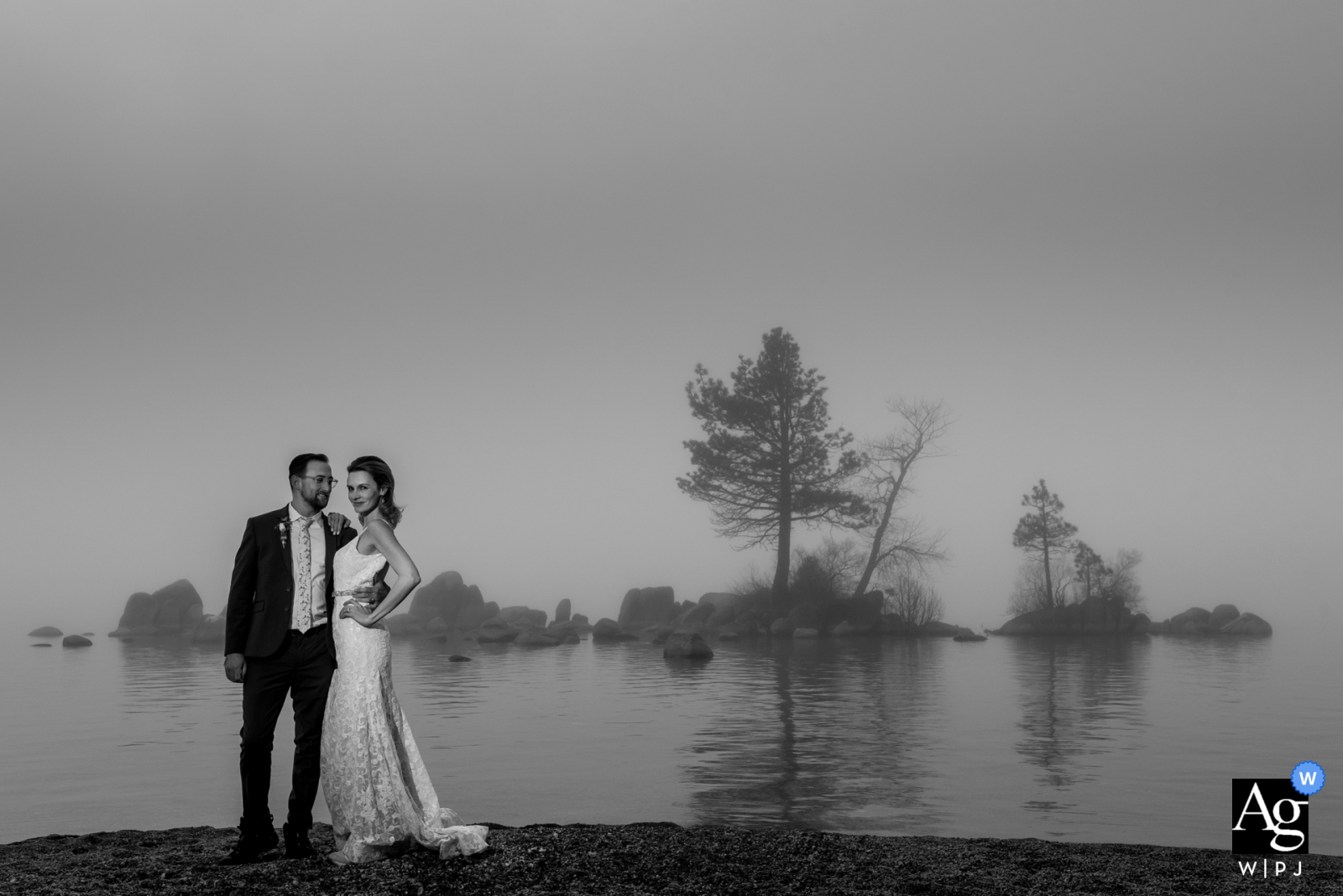 A bride and groom pose on the shores of Lake Tahoe, Zephyr Cove, surrounded by thick fog. 