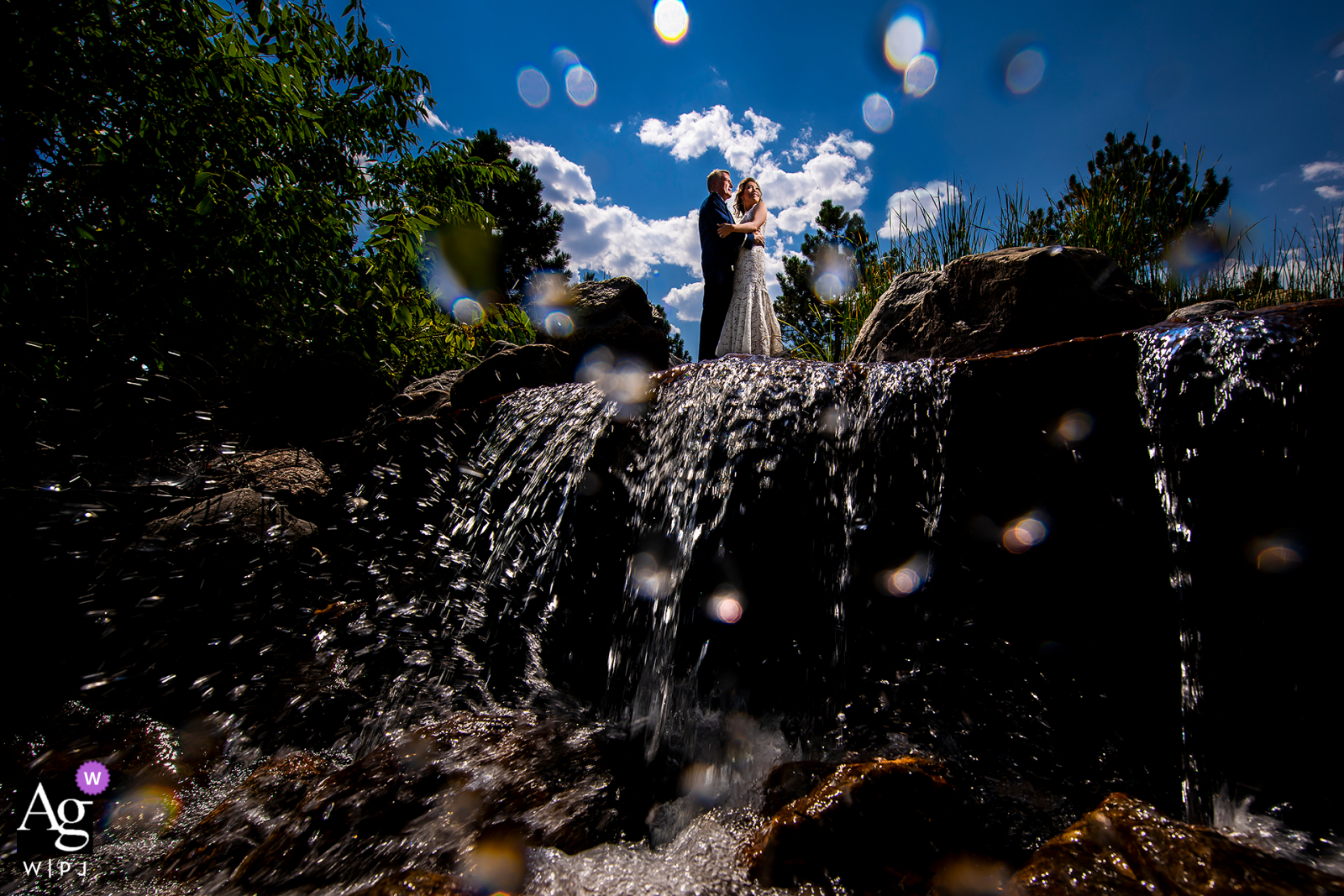 Bride and groom standing on top of waterfall at Spruce Mountain Ranch in Larkspur, CO