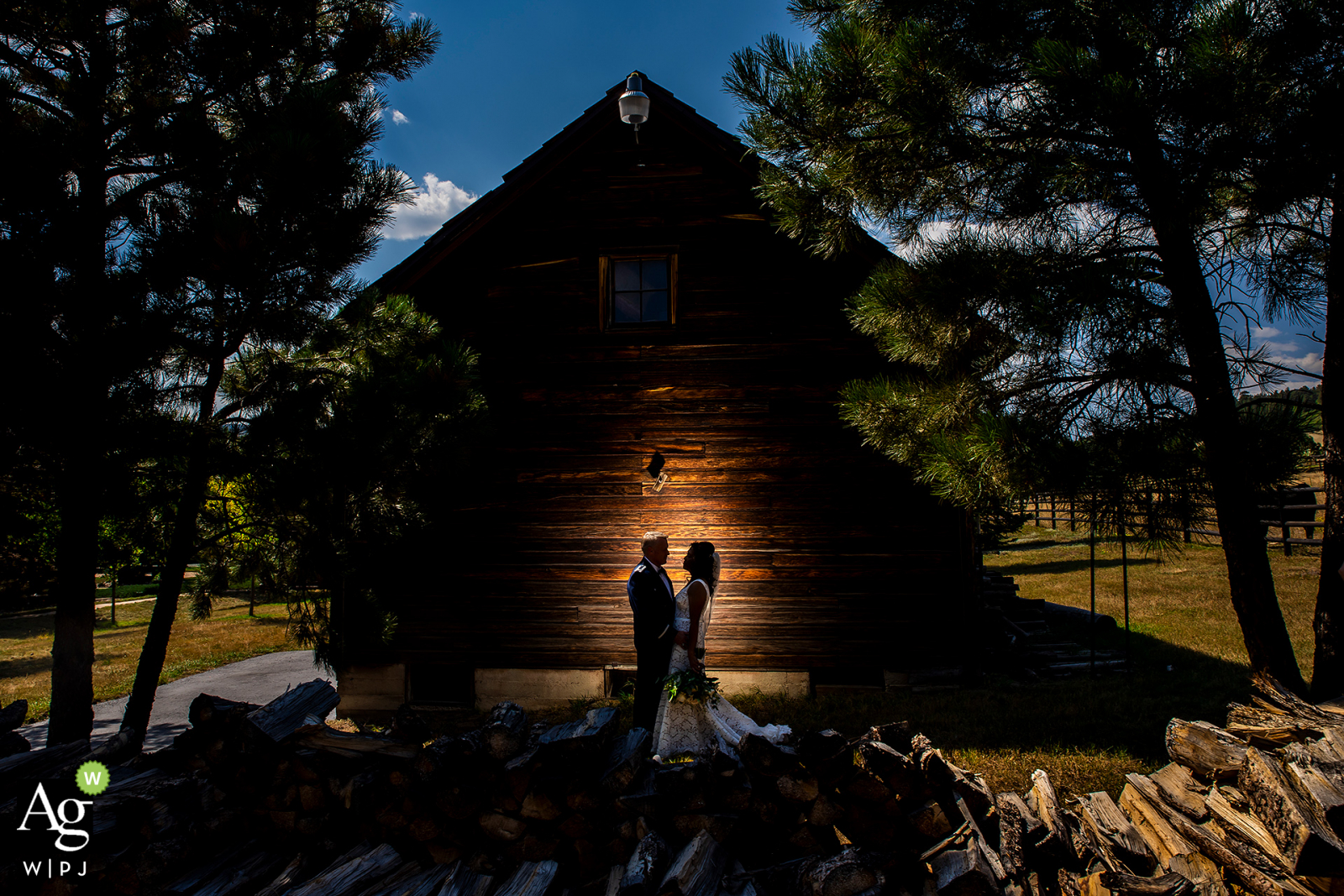 Spruce Mountain Ranch, Larkspur, CO, kreatives Hochzeitsporträt der Braut und des Bräutigams, die neben einer beleuchteten rustikalen Scheune stehen