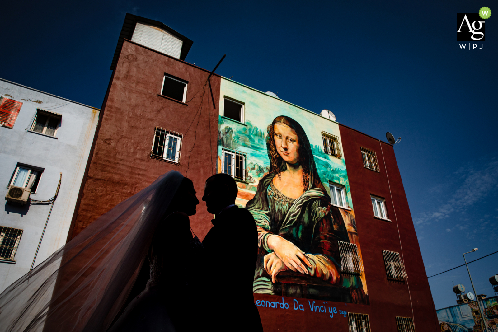 Mersin, Turkey fine art wedding portrait image of the couple in backlight posing in front of the Mona Lisa painting on a building
