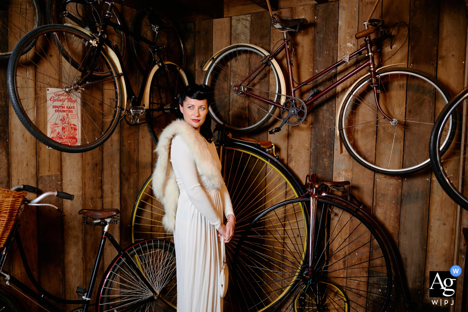 Sessão criativa de retratos de noiva de casamento em Hampshire, Inglaterra, em tons quentes, contra uma parede de madeira com bicicletas penduradas