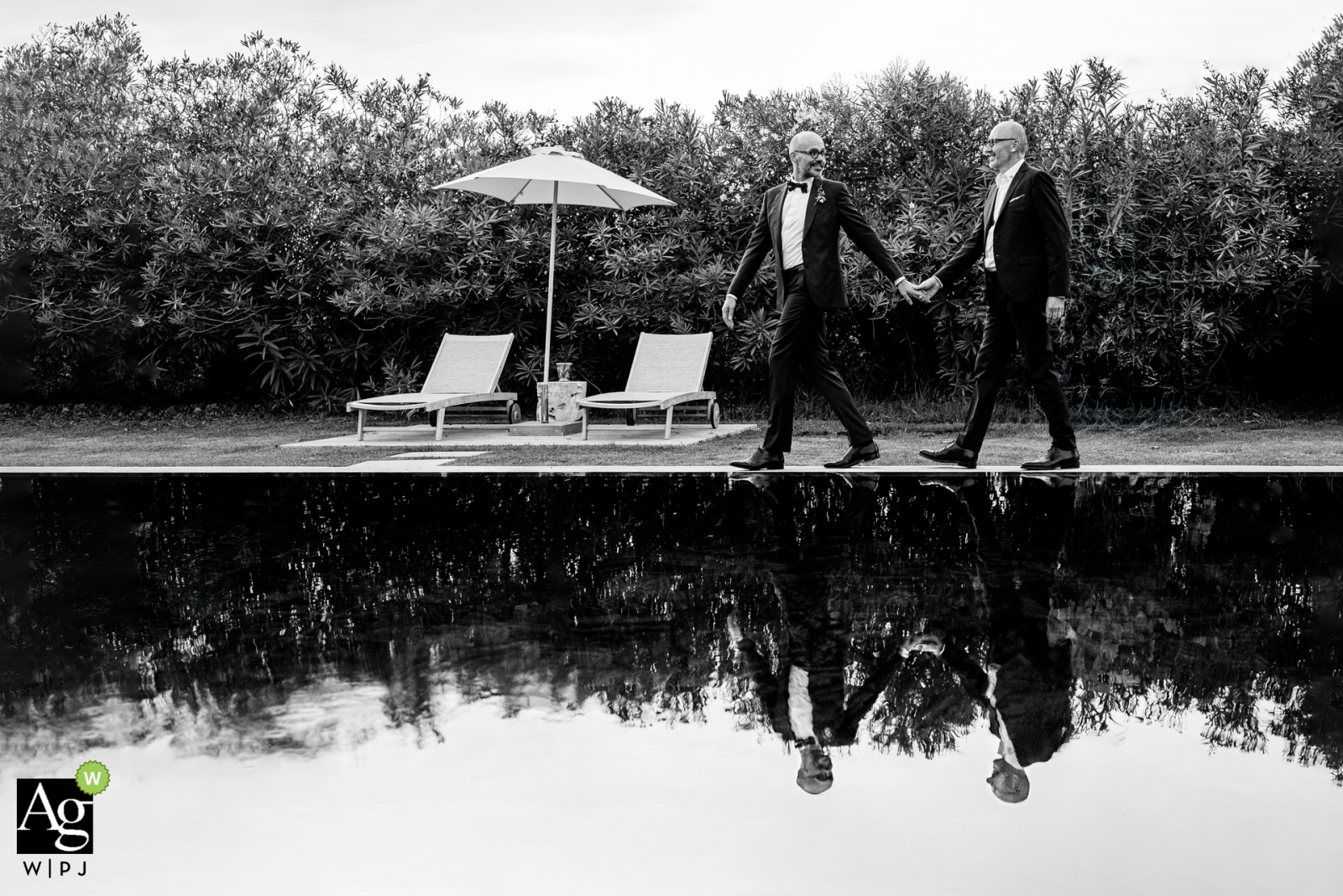 Black and white portrait by the pool at Domaine de la Trinité in Mauguio, Herault. The couple's hands are interlaced, with their reflection visible in the water beneath them.