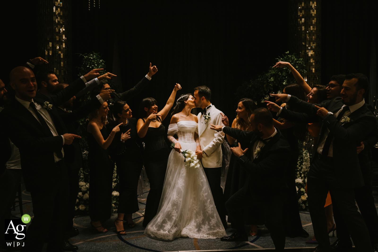 In the beautiful setting of Mersin Hilton Hotel, a joyous wedding scene unfolds at night as the bride and groom share a heartfelt kiss, surrounded by their loving friends.