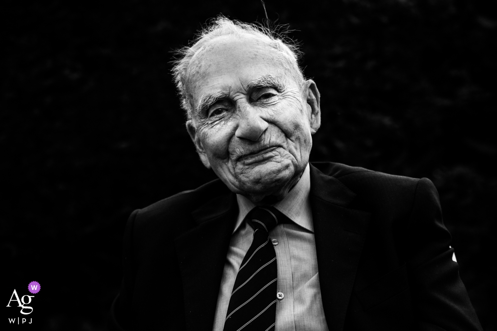 Wedding portrait of the grandfather at Loiret reception venue in Centre-Val de Loire. Grandfather looking into camera against a black background.
