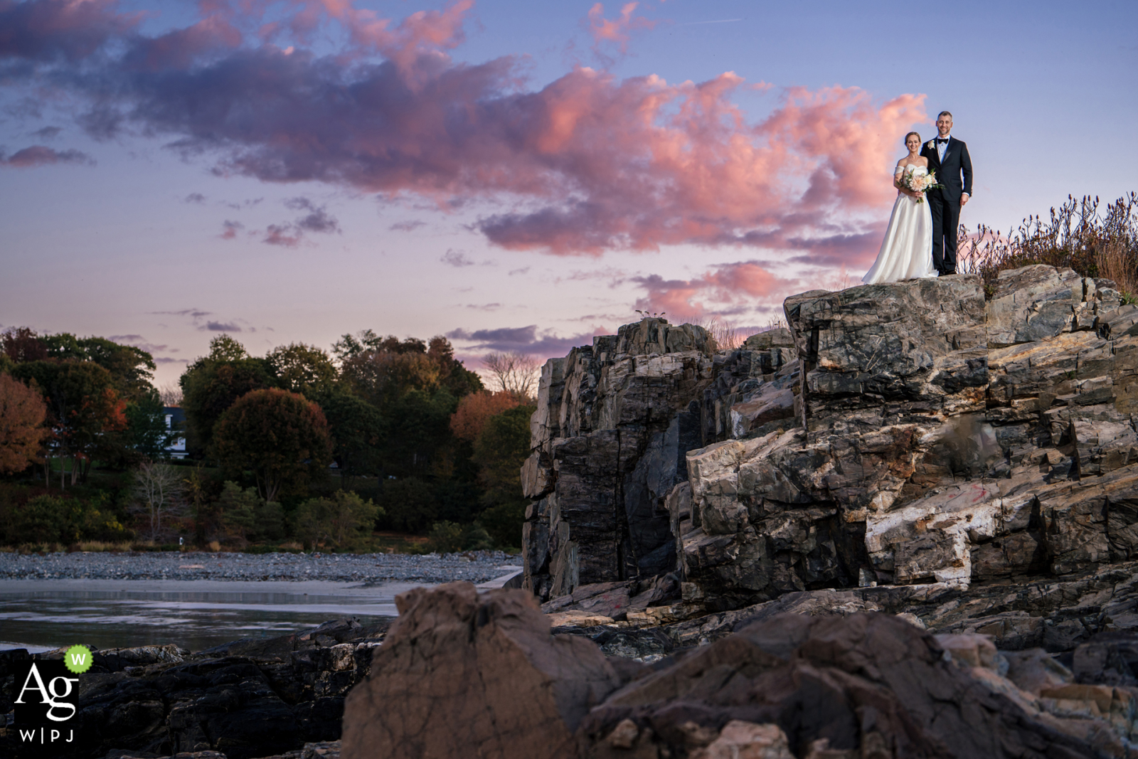 The bride and groom stand on a jagged, rocky cliff overlooking the ocean at Stage Neck Inn, York, Maine.