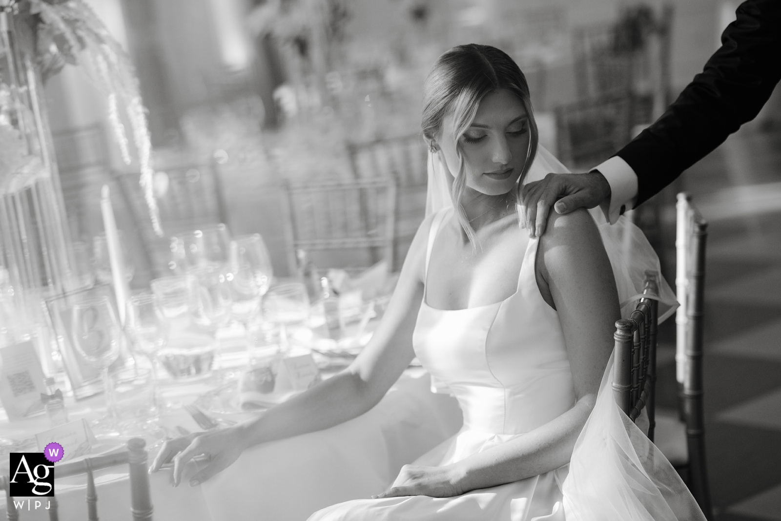 At Terra Residence, Sofia, an intimate portrait captures the bride seated on a chair, with a close-up detail of a man's hand gently resting on her shoulder, conveying warmth and connection.
