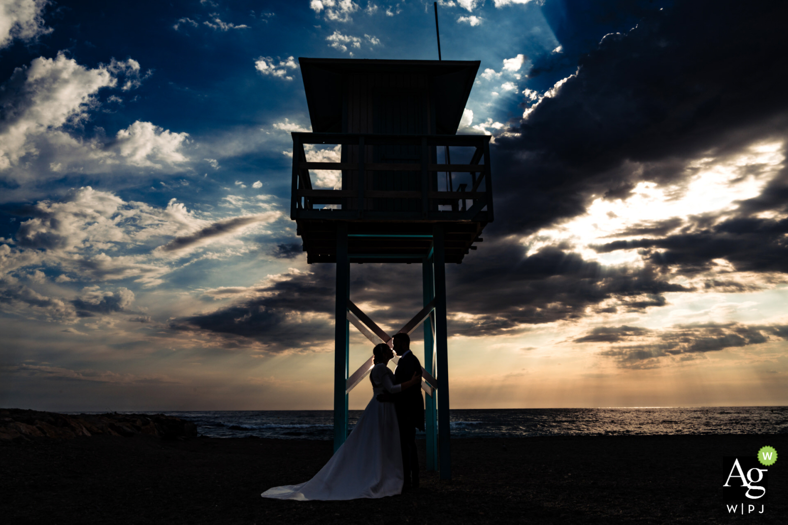 Bride and groom portrait in Torrenueva, Granada, Spain, after sunset, with a beautiful sky, ocean, and lifeguard stand in the background.