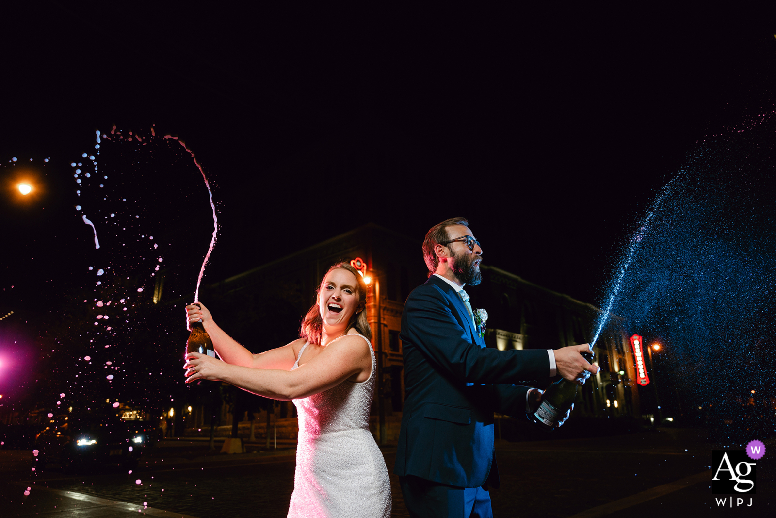 In Milwaukee, Wisconsin, the couple creates an unforgettable night shot, popping two bottles of champagne while vibrant colored lights dance in the background, capturing the festive energy of their celebration.