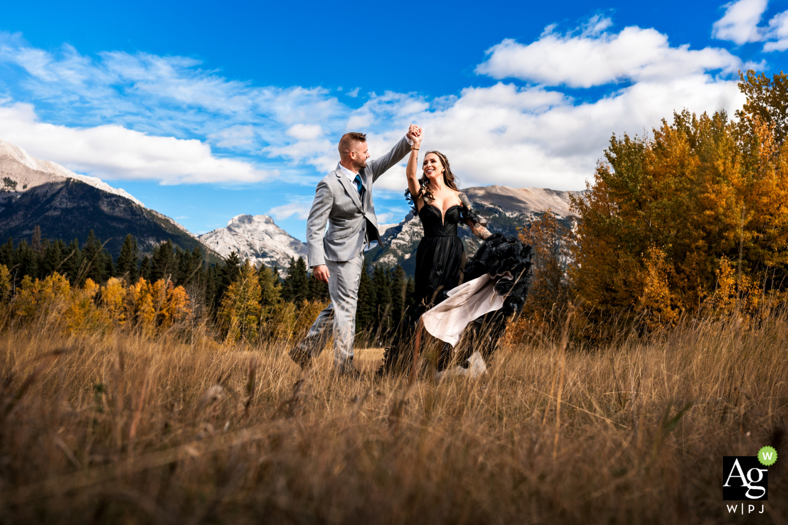 A bride in a black wedding dress and her groom dance amidst the fall colors in the mountains near Canmore, Canada.