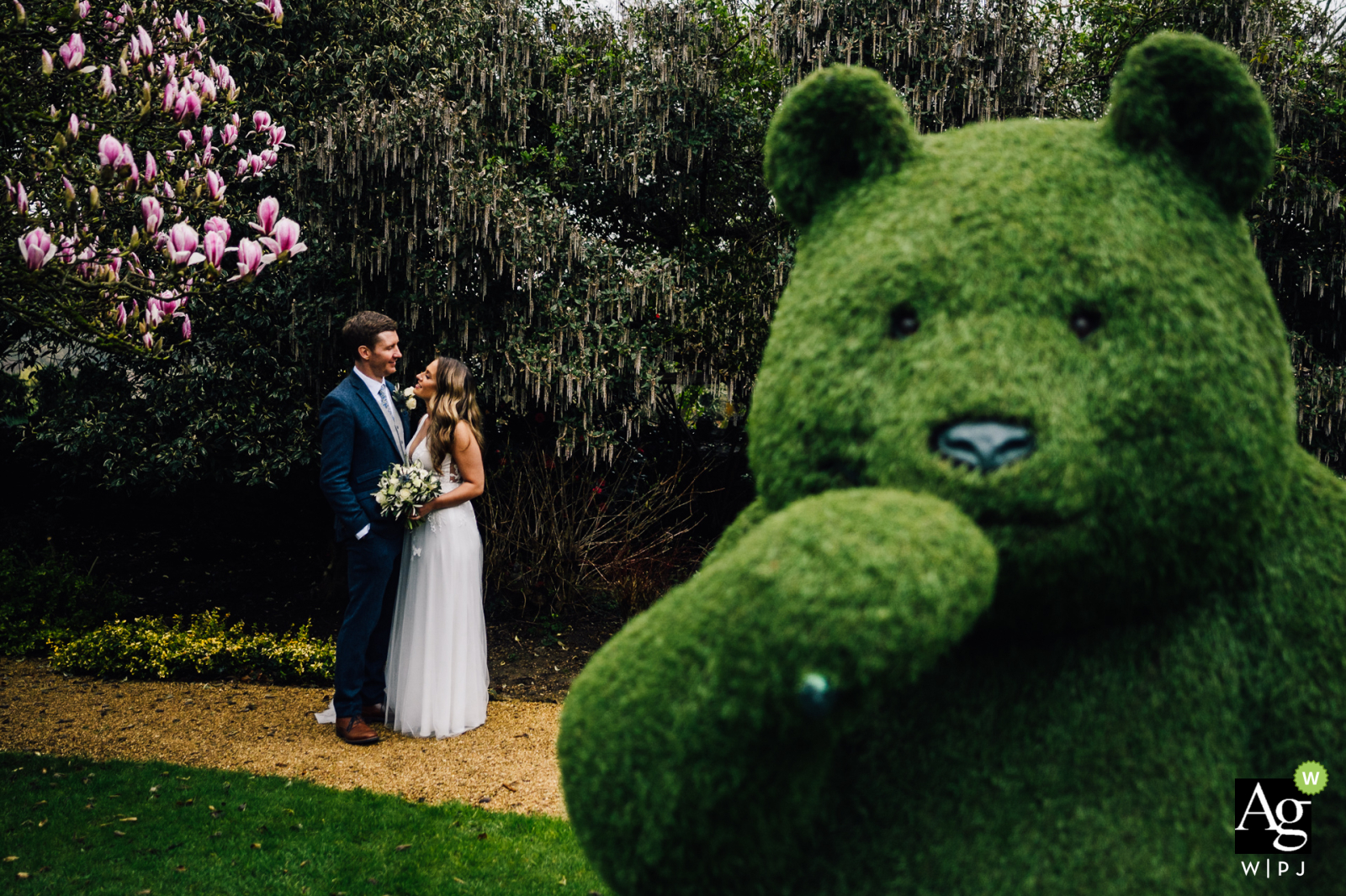 Newlyweds stand at Homewood, Bath, with a whimsical topiary teddy bear part of their wedding portrait