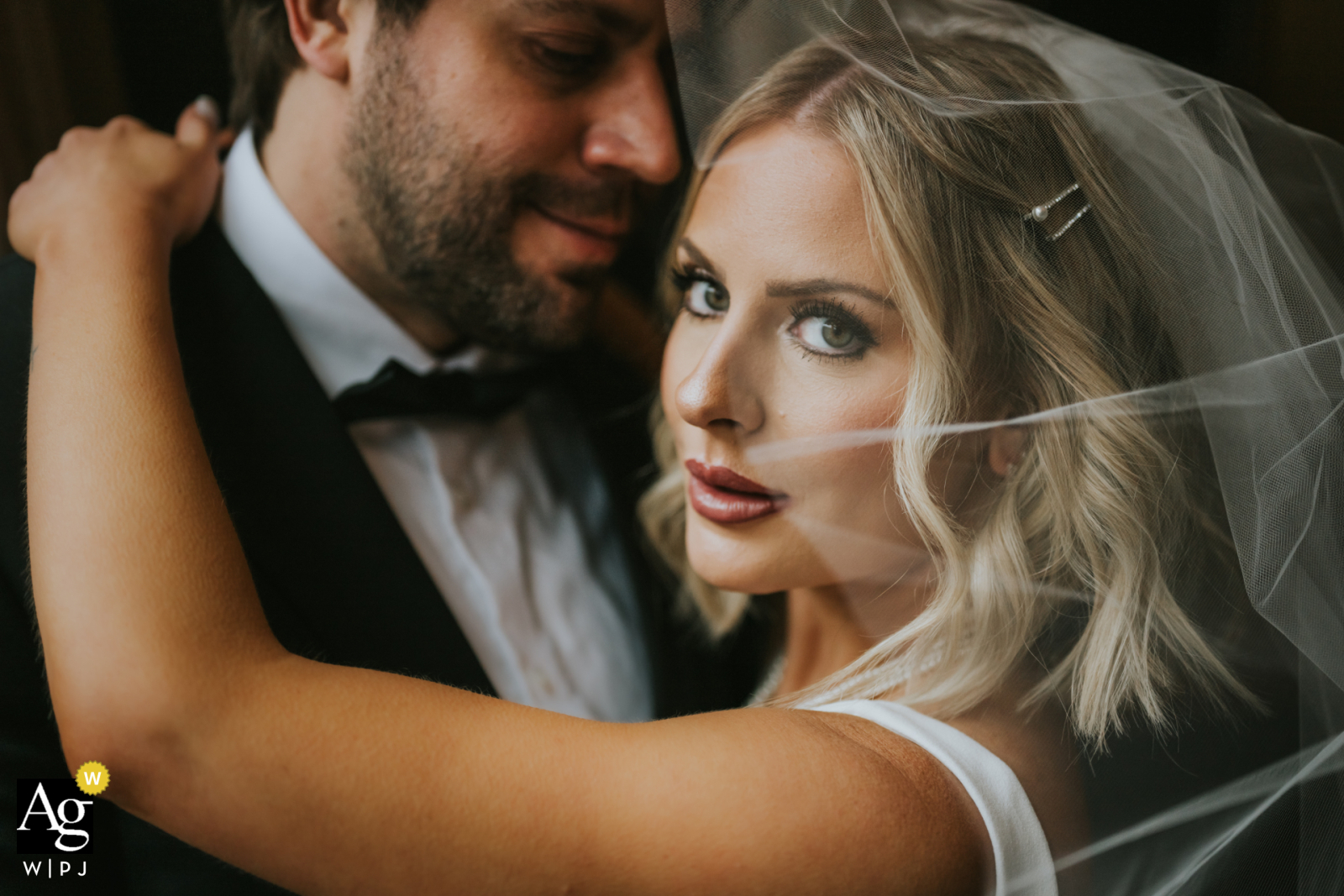 In a Cleveland, Ohio hotel, an impromptu photo captures window light highlighting the scene. The bride rests her hand on the groom's shoulder and gazes intensely at the camera, creating a powerful and captivating image.
