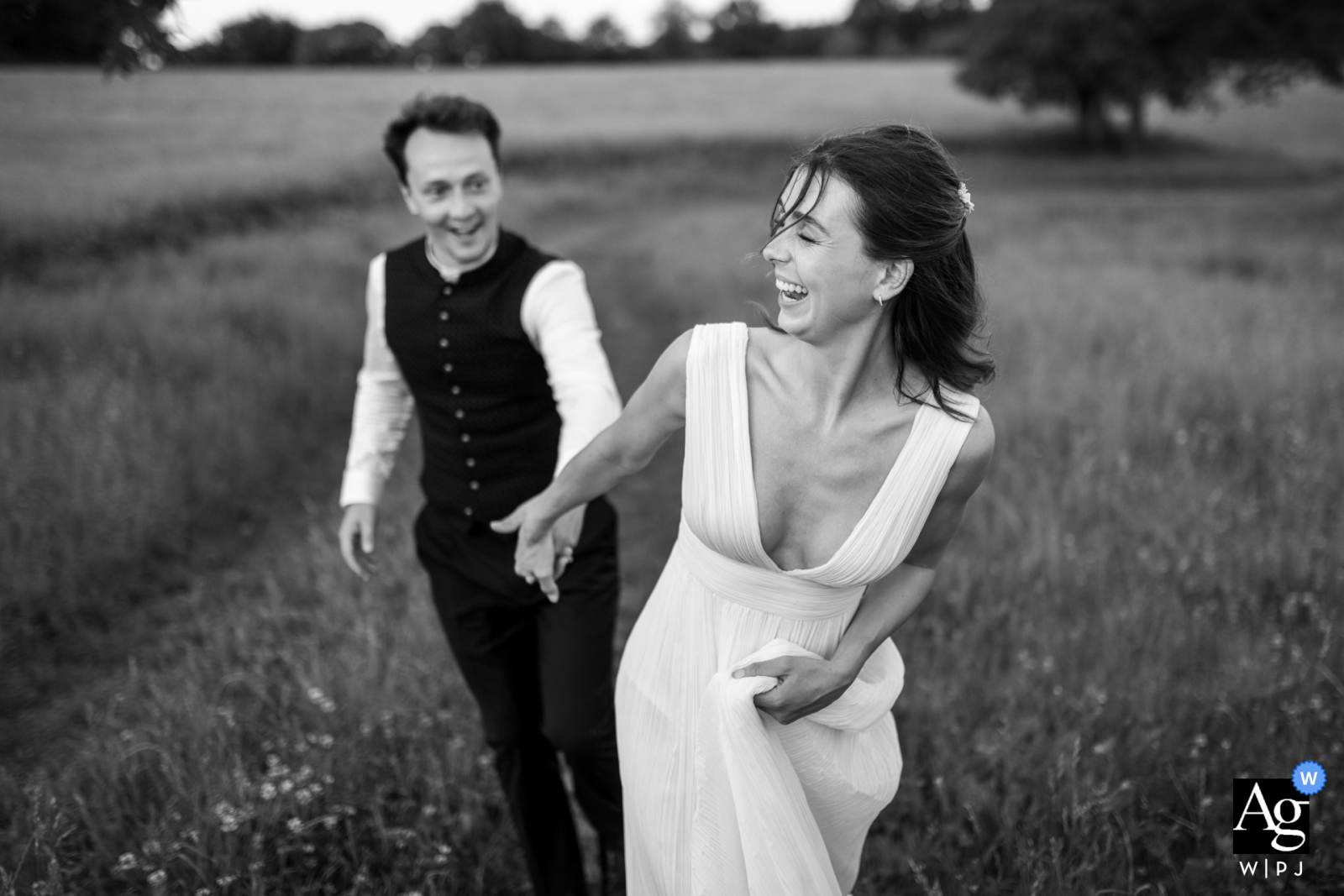 Black and white shot of the married couple running hand-in-hand through fields in Charente, France.