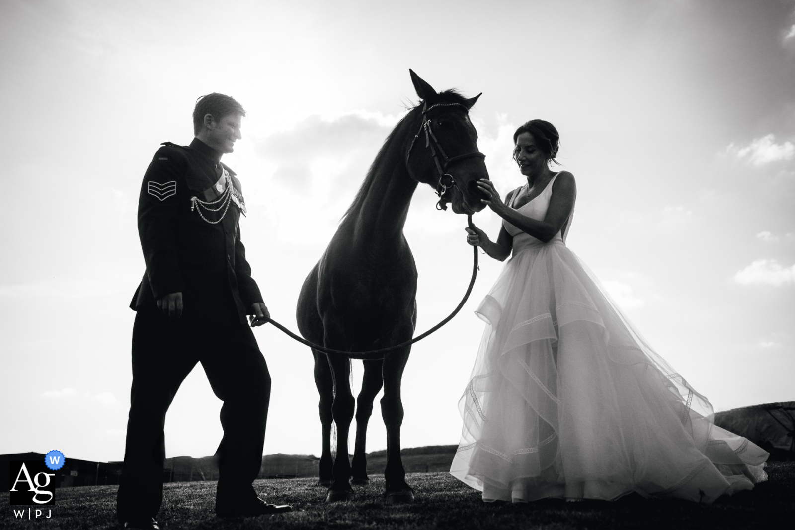 An artistic black and white wedding portrait of the bride and groom at her Dorset, England home, standing thoughtfully with their horse.