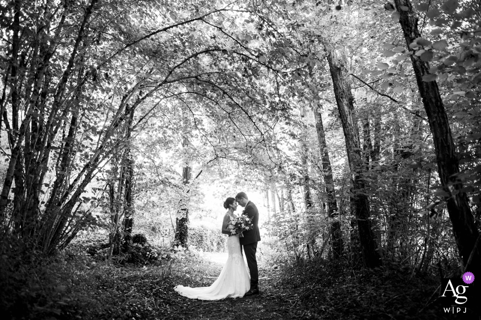 Bonneuil Matours, France — The couple poses in the Moulière forest for a symmetrical black-and-white portrait, with the arching canopy of trees creating a dramatic and natural overhead frame.