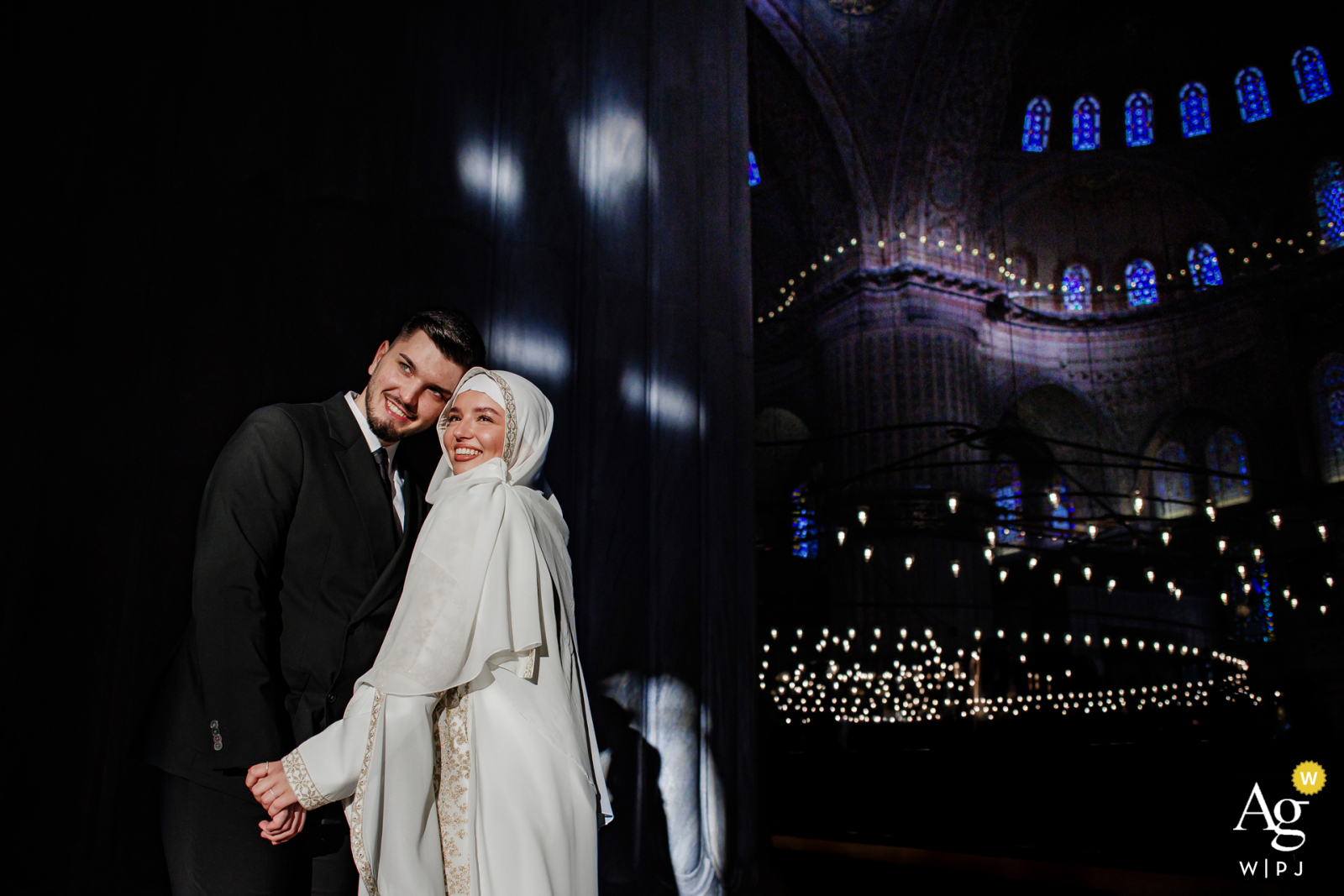 Blue Mosque, Istanbul, Türkiye — Indoors in low light, the bride and groom pose cheek to cheek, softly illuminated by the photographer, creating an intimate and romantic wedding day portrait amid the historic setting.