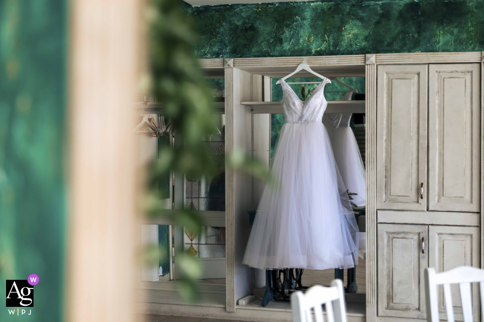   In a rustic hotel room in Budapest, a delicate wedding dress hangs in quiet anticipation, ready for the start of a memorable day.