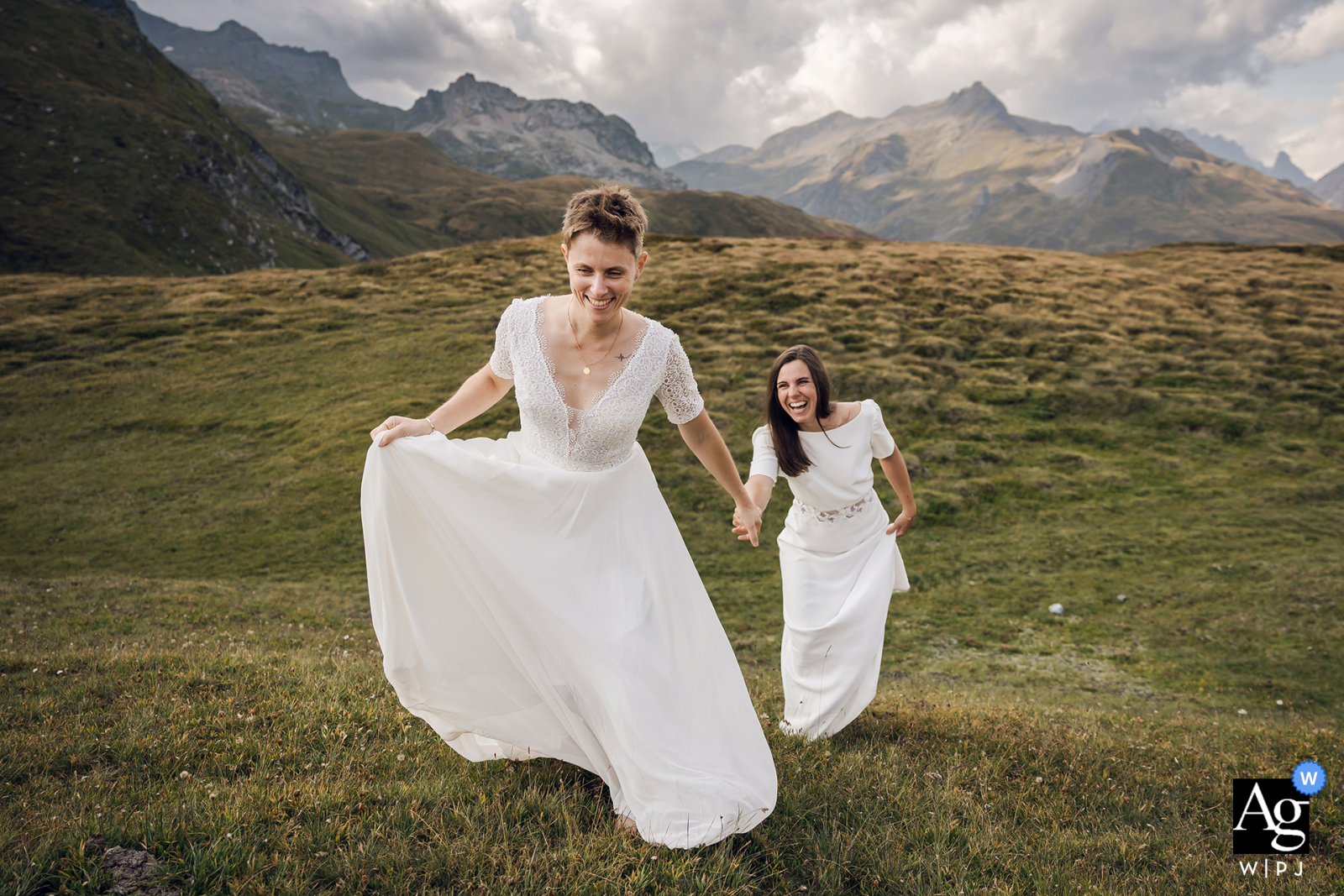 High In The Mountains, The Couple Runs Up A Slope While The Landscape Adds Vibrant Energy To The Scene In the mountains, the couple are pictured during their photo session as they run back up a slope, the surrounding landscape creating a vibrant and dynamic wedding scene.