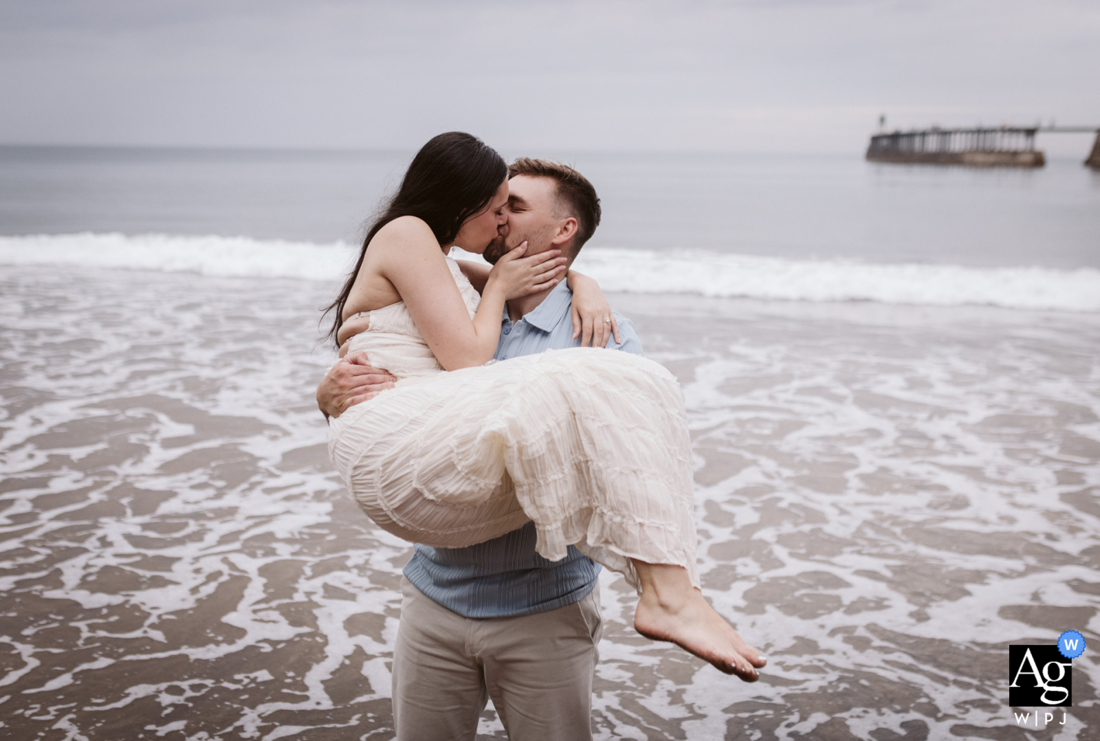 Newlyweds Share A Kiss On Whitby Beach Where They Got Engaged, Waves And Sand Creating Romance By The Sea On the beach at Whitby, the newly married couple shares a kiss at the spot where they got engaged, with waves and sand creating a romantic seaside scene.