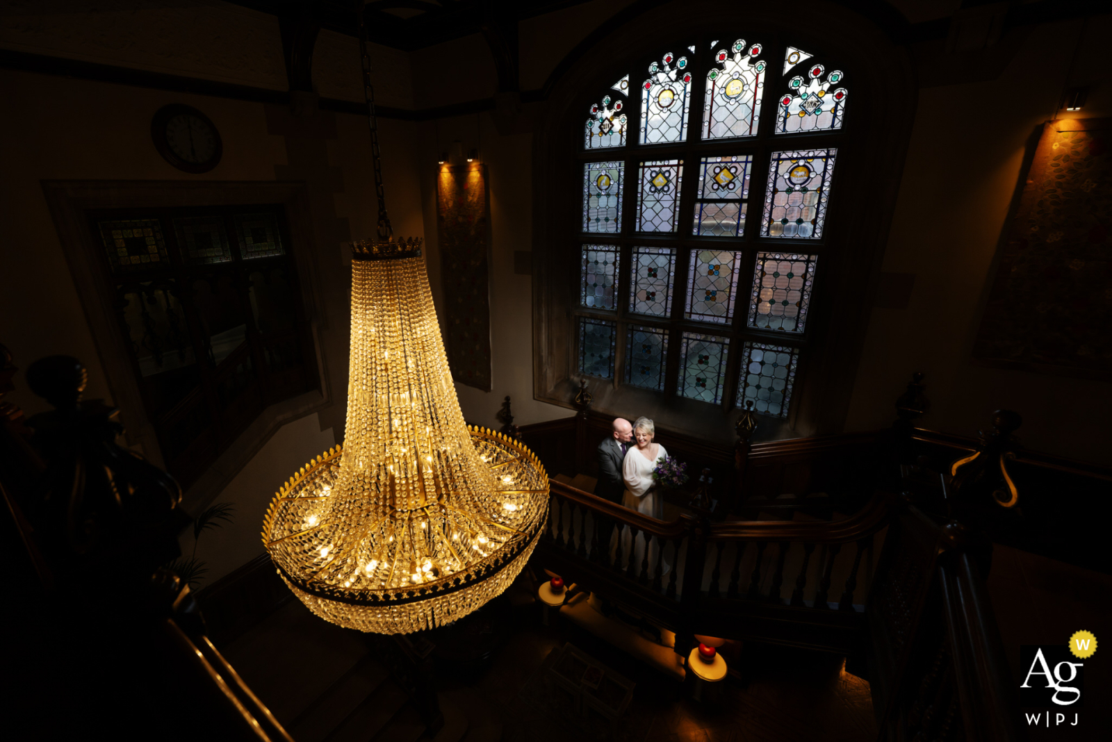   On the grand staircase at Pendley Manor, the couple pose for a portrait, the sweeping stairs and ornate railing showcasing the manor’s classic elegance.