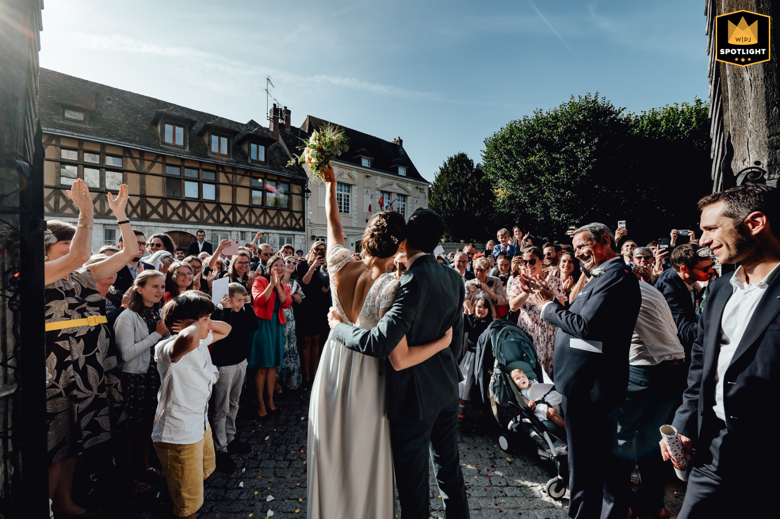 Newlywed couple walking out of Église Saint-Sauveur du Petit-Andely in France, greeted by guests applauding and celebrating their marriage.