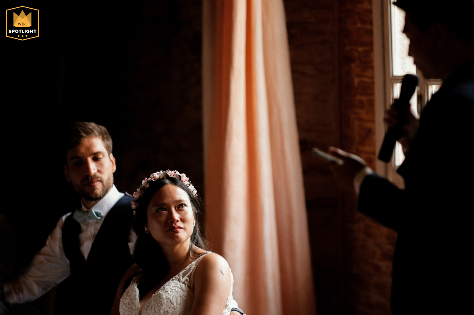 Château Malvirade Wedding: Emotional Bride and Groom Captivated by Family Speech At Château Malvirade in Lot et Garonne, the bride's eyes are filled with emotion as she sits with the groom, both looking up at the woman giving a speech.