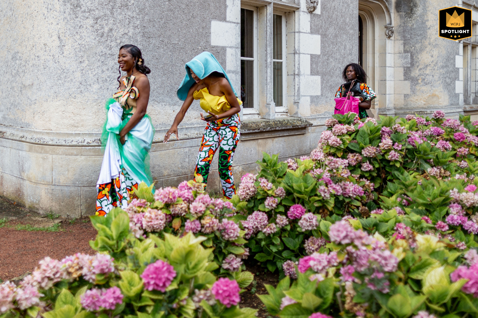 Un moment de mariage en plein air capturé au Château de Périgny, 86190 Vouillé, où la mariée et ses deux témoins se dirigent vers la cérémonie, l'un utilisant une serviette pour se protéger de la pluie, tandis que l'autre porte un kit de maquillage dans une photo documentaire légère.