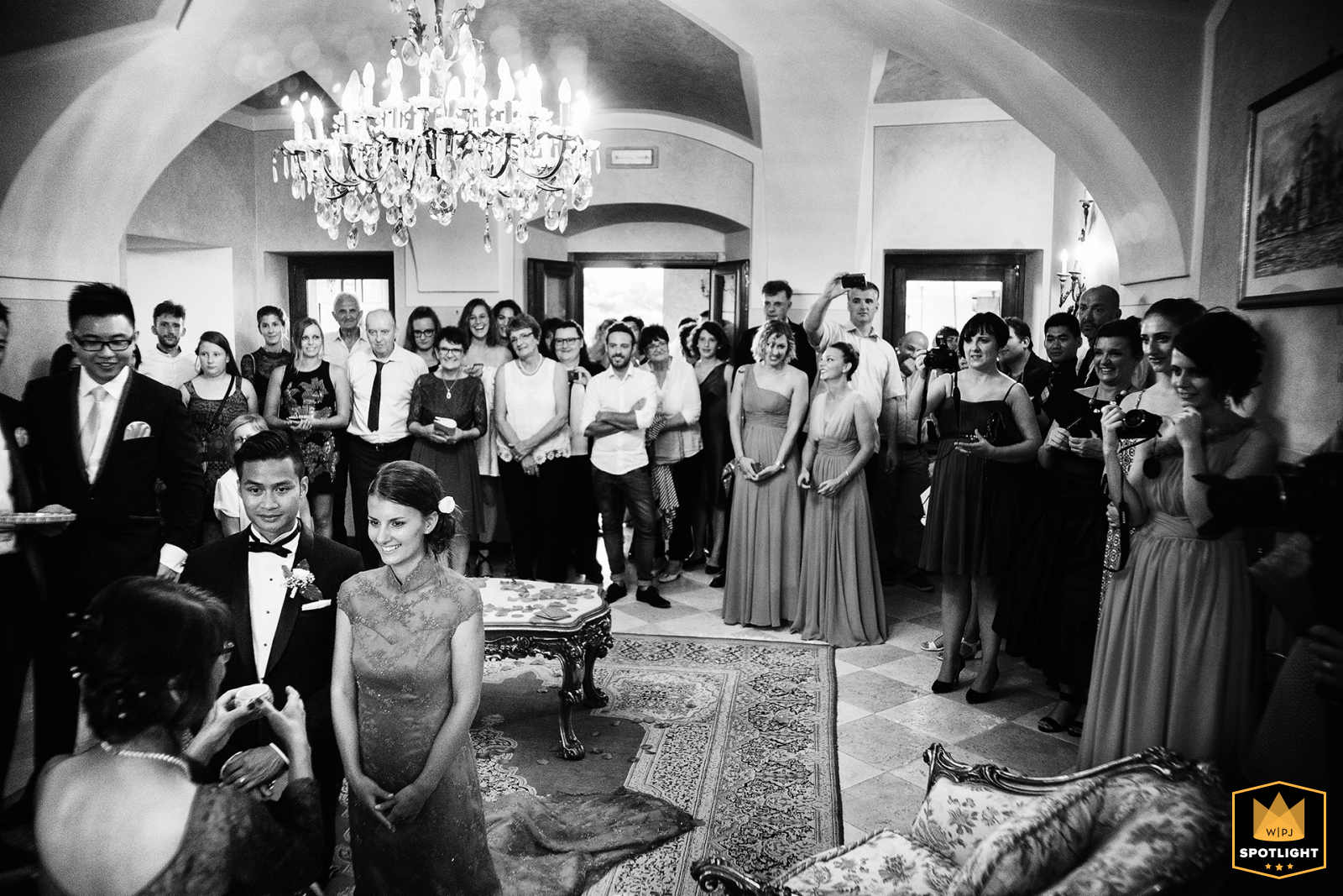 A heartfelt black and white wedding photo captured at Villa Avanzi in Polpenazze del Garda, showing a tender tea ceremony moment as the newlyweds offer tea to their parents, surrounded by guests in a setting by Garda Lake.