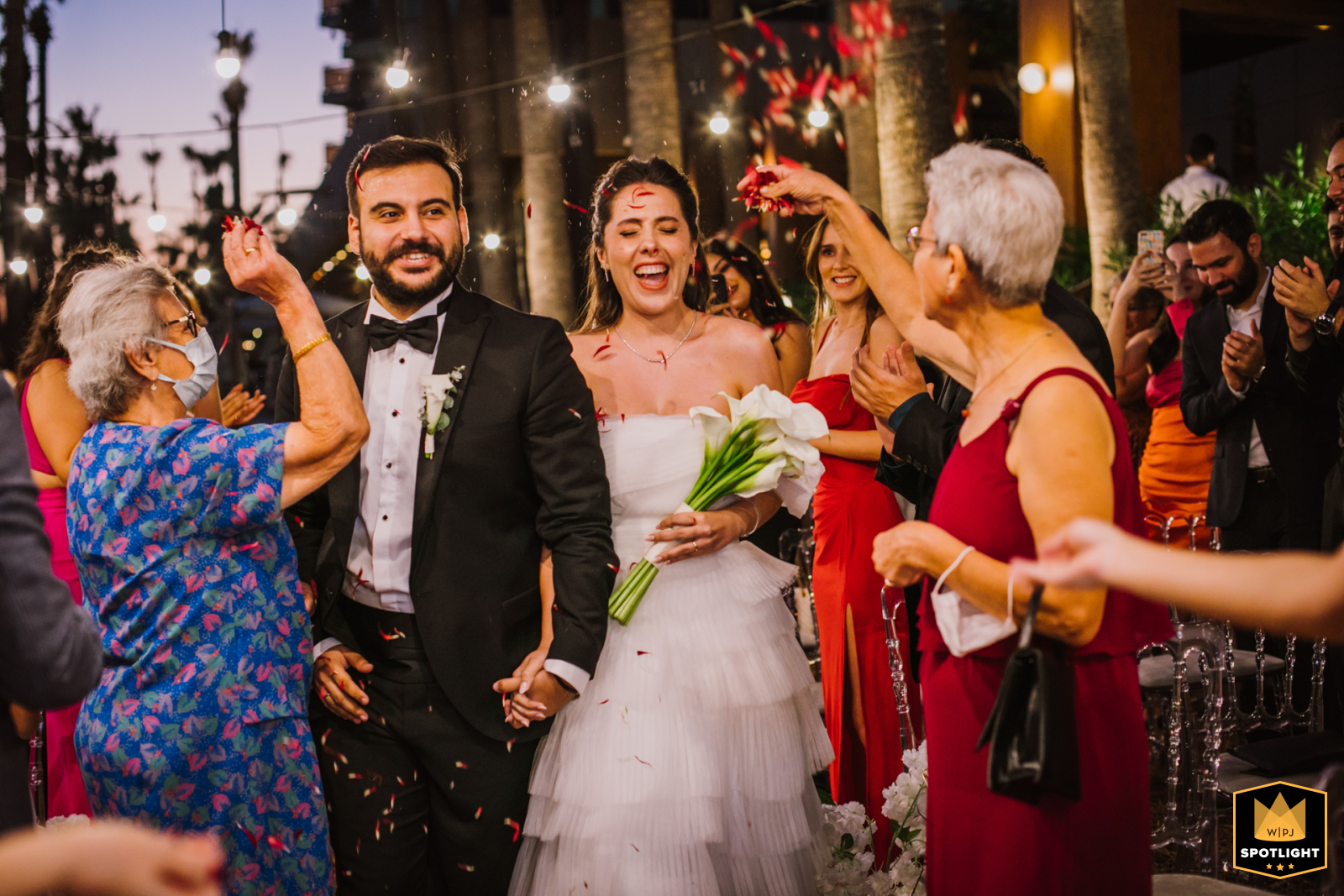 Petal Path of Love: Newlyweds Embrace amid Flower Shower at Hilton Hotel Mersin A beautiful moment captured at a wedding venue, as the bride and groom smile while taking their first steps together amidst a cascade of petals thrown by joyful guests at the Hilton Hotel in Mersin.