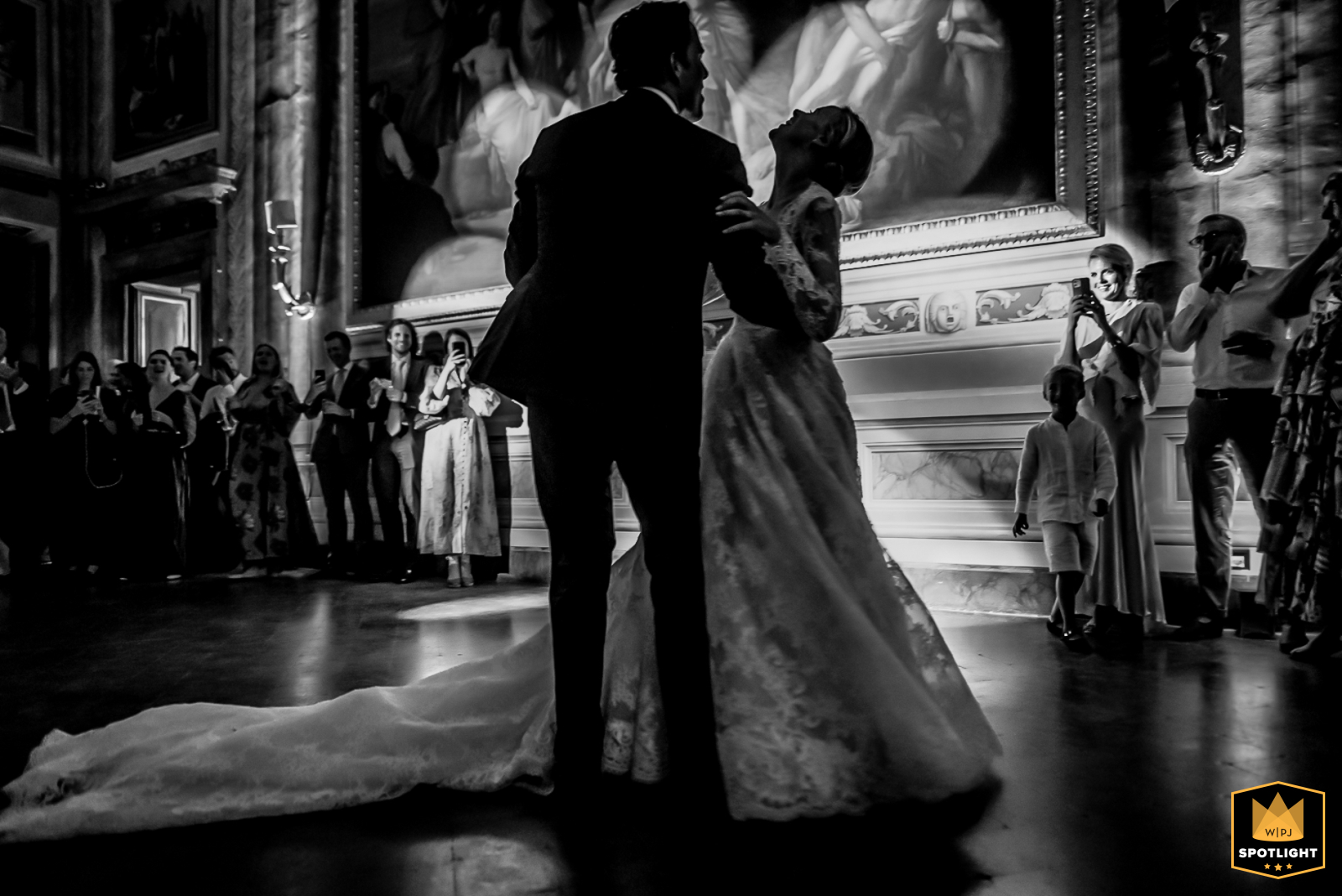 At Villa Mansi in Segromigno in Monte, the bride and groom share their first dance in the grand ballroom, surrounded by friends and relatives, radiating love and joy.