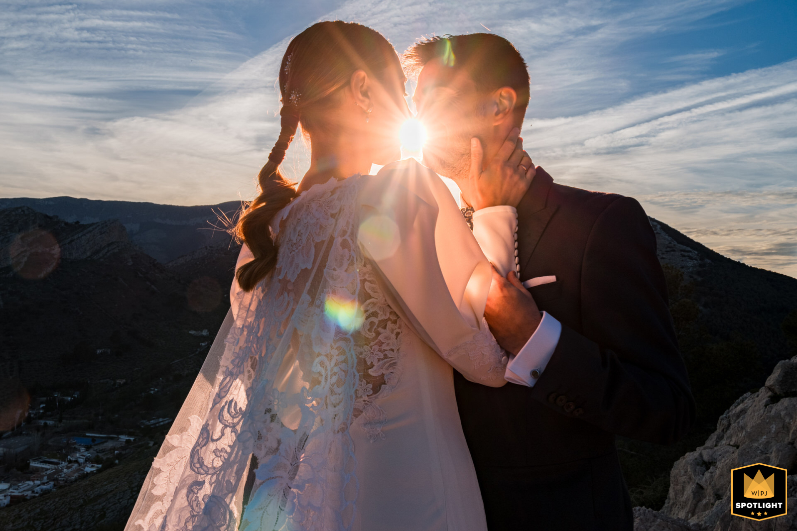 In Jaén, Spain, a couple stands together before dusk with the sunset shining brightly between them as they prepare to share a kiss.