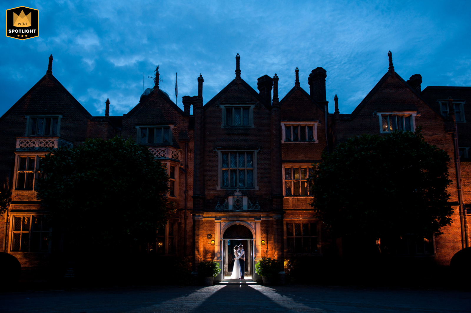 Elegant Romance at Great Fosters: A Silhouetted Blue Hour Portrait of a Blissful Couple At the historic Great Fosters in Eggham, Surrey, the happy couple is captured in a dreamy blue hour photo, silhouetted against the grand doorway by their skilled photographer.