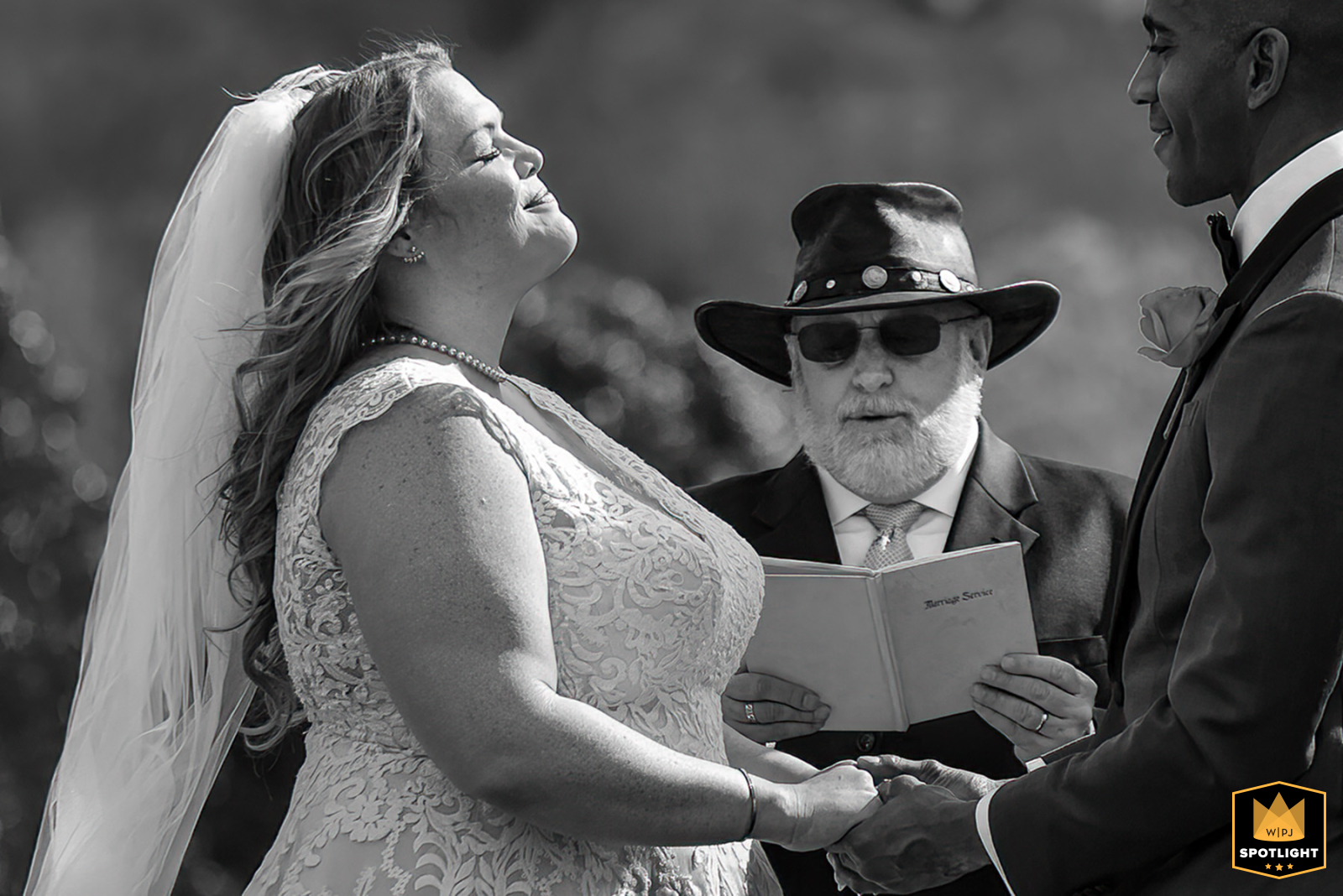 A sunny outdoor wedding at Aska Farms in Blue Ridge, GA. The bride and groom hold hands and the bride smiles with her head back during the ceremony.